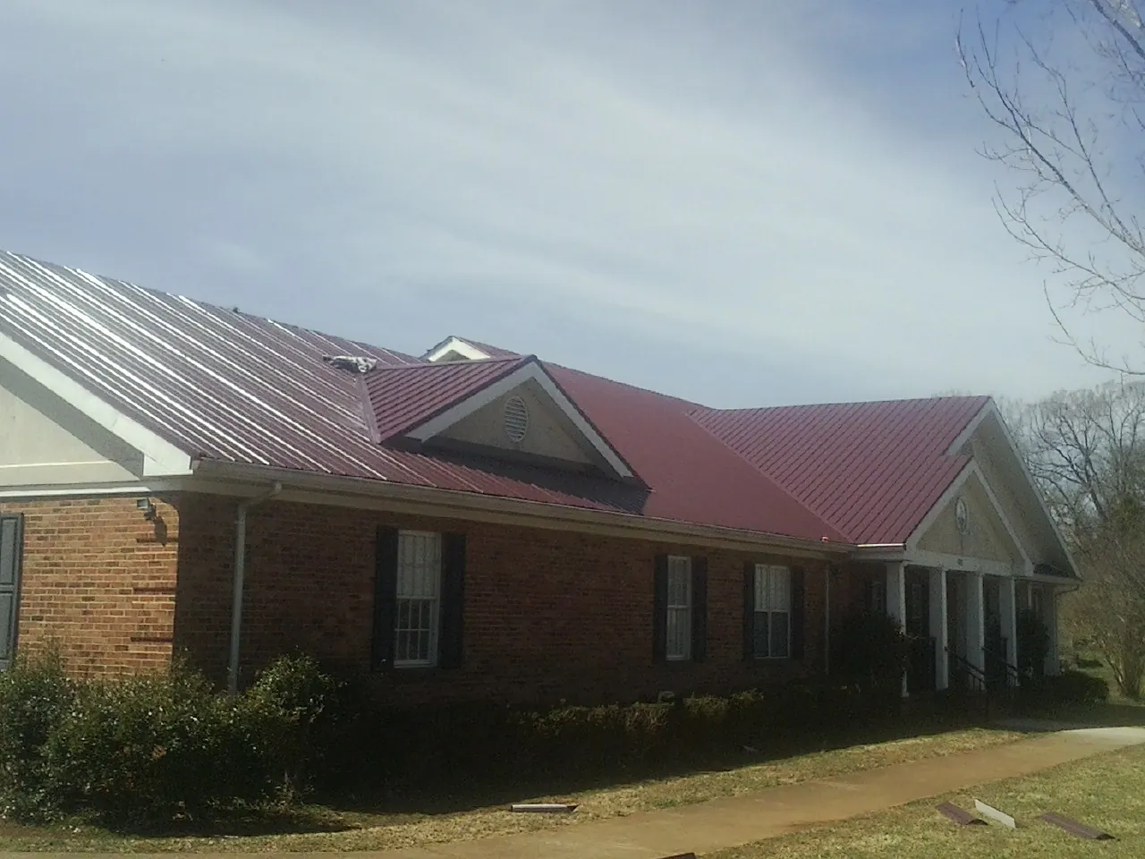 Red metal roof with gabled entries on a long brick building, from a Hail Damage Roof Repair job in Franklinville